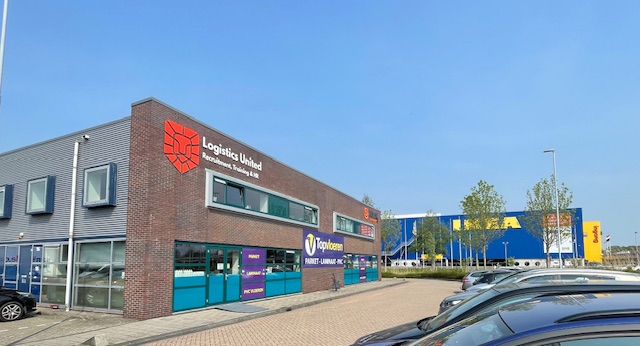 Een foto van een nieuw kantoorpand met een gloednieuw logo op de gevel. Mensen zijn bezig met klussen, zoals het sausen van muren en het plaatsen van houten panelen. Een spreekkamer met glazen wand wordt voorbereid voor gebruik.
